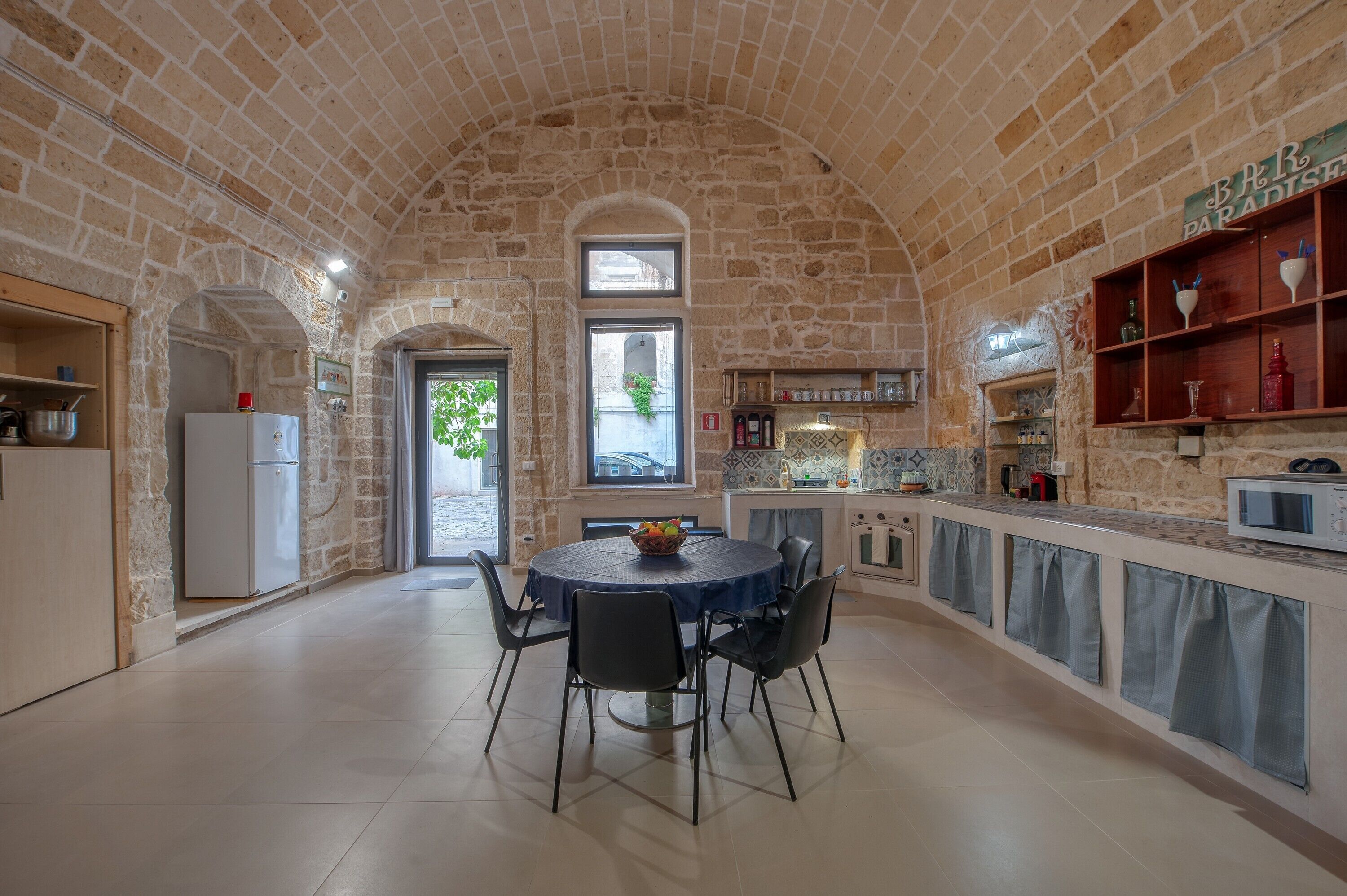 Una cocina de paredes de piedra con una mesa redonda de comedor, sillas y un refrigerador.