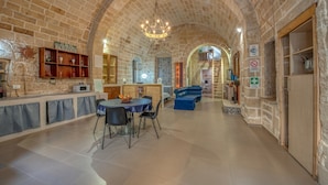 Een ruime binnenruimte met een hoog gewelfd bakstenen plafond, een eethoek met een ronde tafel en stoelen, en een blauwe bank.