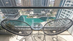 Un balcón con dos sillas de mimbre y una mesa pequeña, con vistas a una piscina y un paisaje urbano.