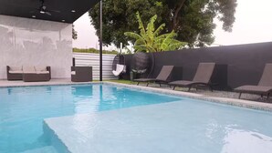 Une piscine avec des chaises longues et un espace salon abrité.