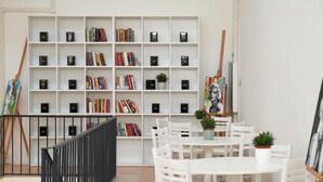 Een kamer met een witte boekenkast vol boeken, een witte tafel met stoelen, en een schilderij aan de muur.