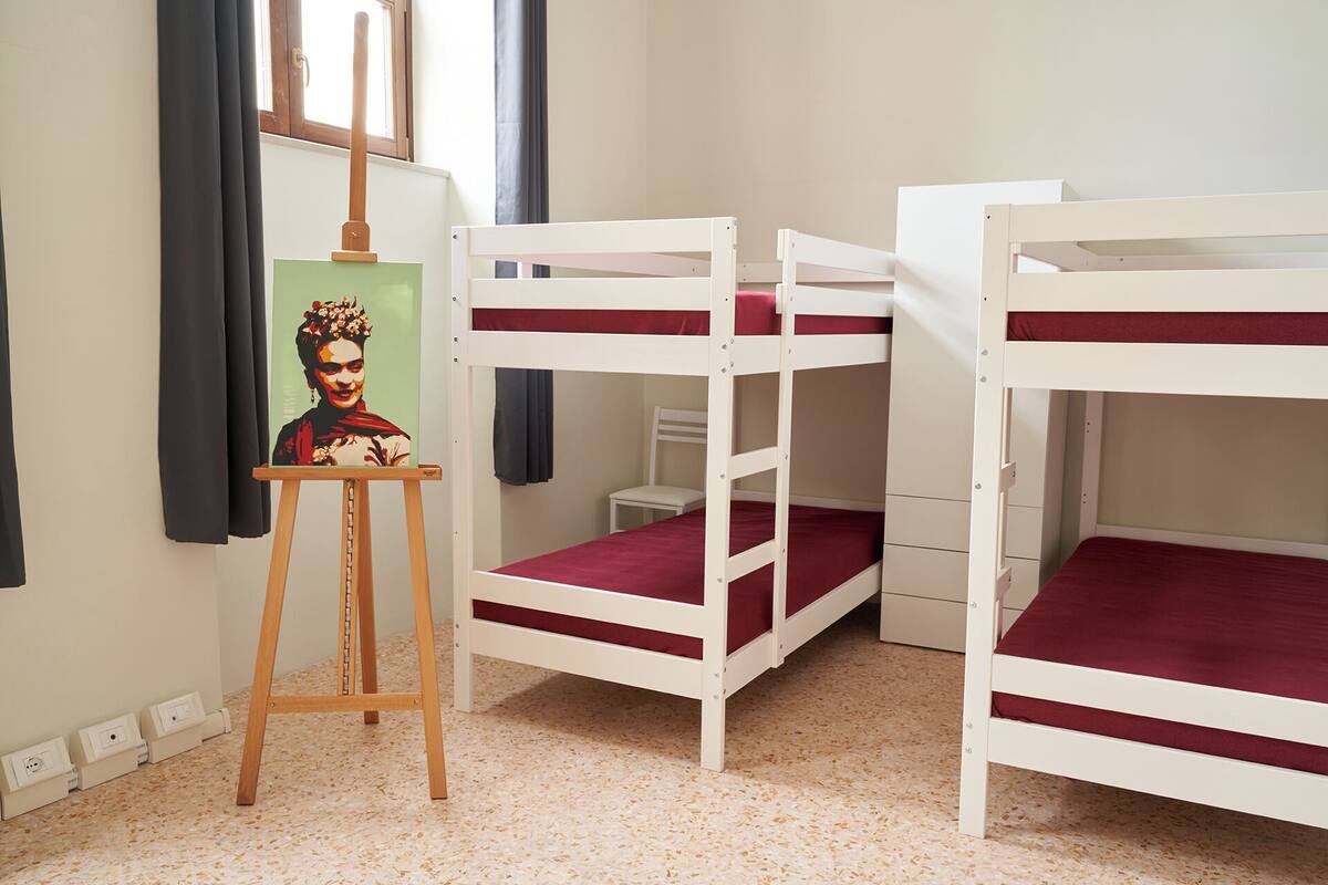 A room with bunk beds, a small desk, and a painting on an easel.