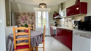 A modern kitchen with red cabinets, a white dishwasher, and a dining area with a wooden table and chairs.