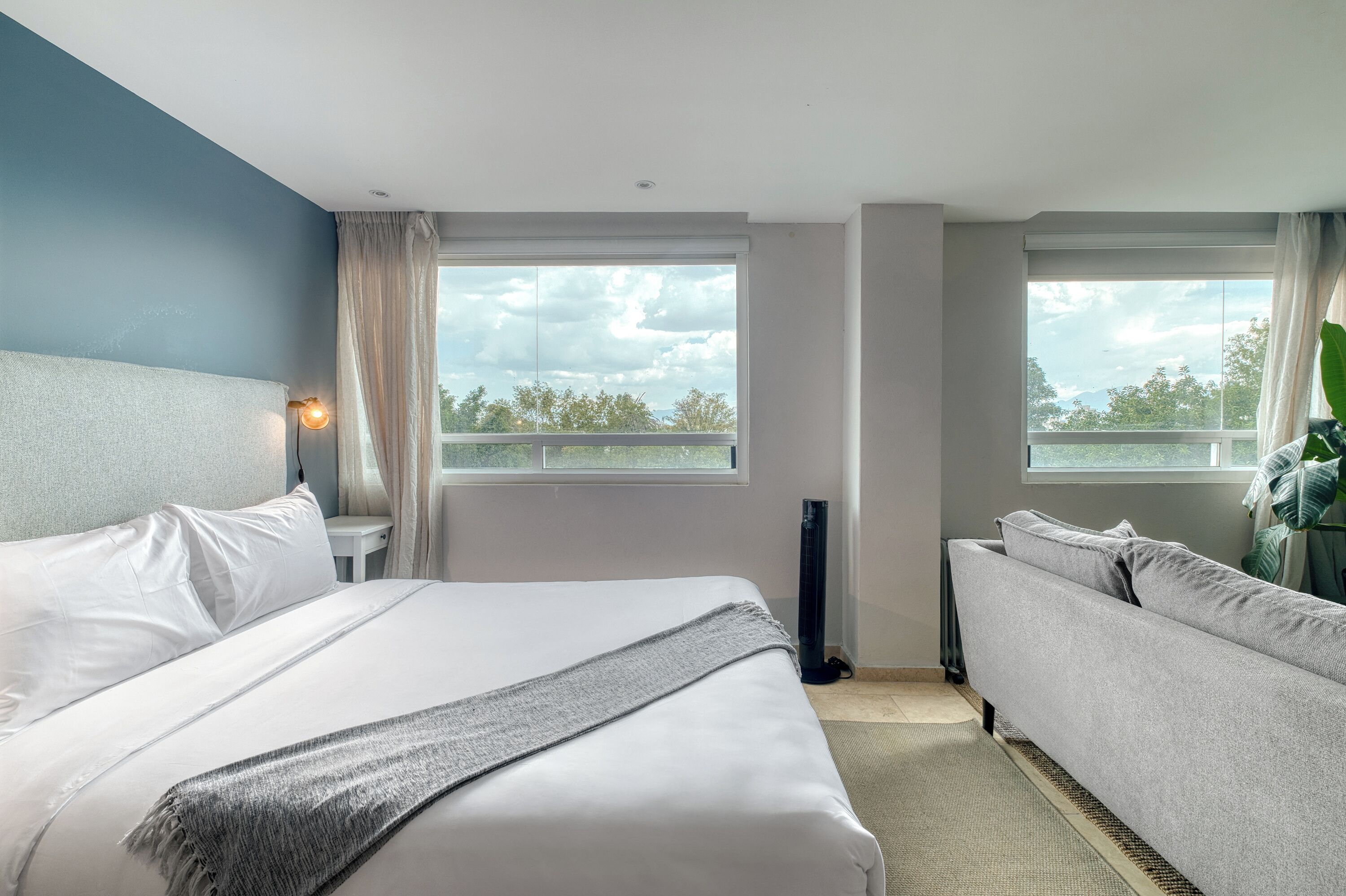 Une chambre d’hôtel avec un lit, un canapé, une fenêtre donnant sur un beau paysage et une table de chevet avec une lampe.