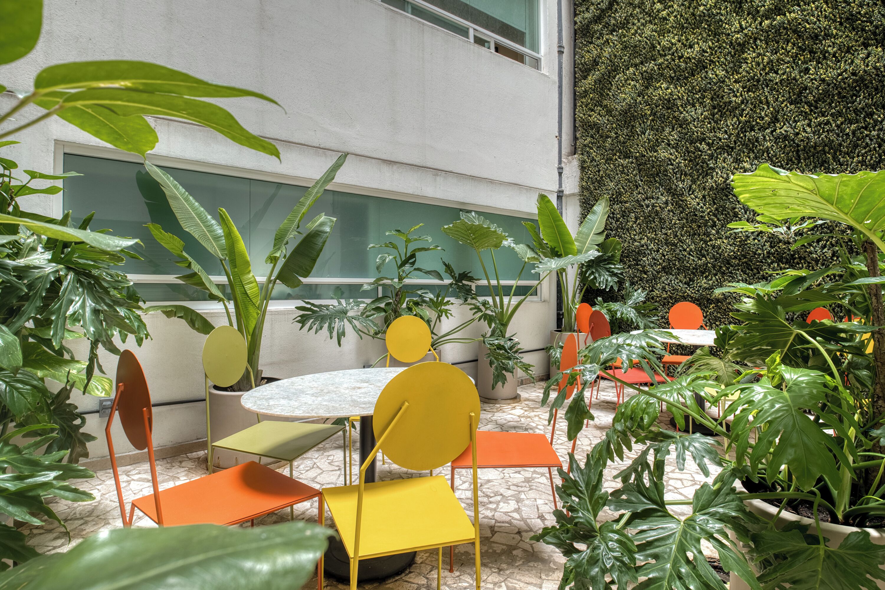 Un espace extérieur aménagé avec des tables et des chaises rondes, entouré de plantes en pot.