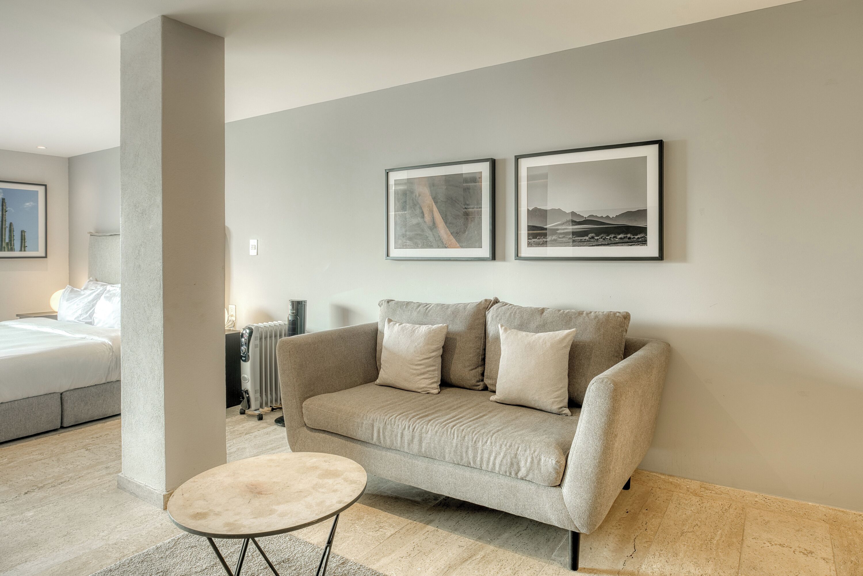 Una sala de estar moderna con un sofá beige, una mesa de centro redonda y dos cuadros en la pared.