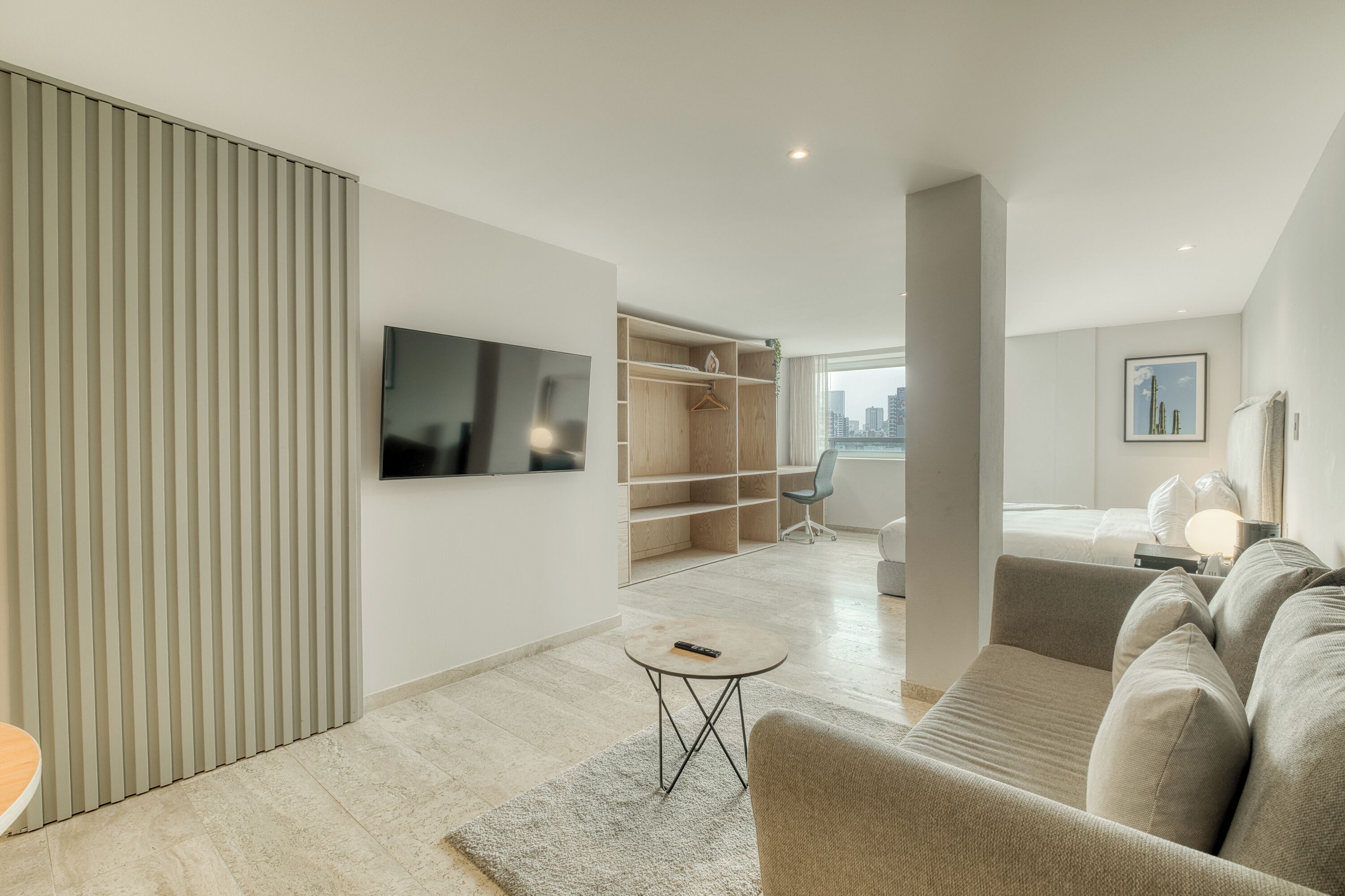 Moderni hotellihuone, jossa on suuri sänky, televisio, oleskelualue sohvineen ja nojatuoleineen, pieni pöytä ja erillinen vaatehuone.