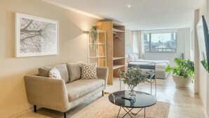 A modern living room with a sofa, a coffee table, and a large window offering a city view. - Nido Roma (Mexico City)