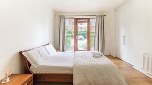 A bedroom with two beds, a wooden headboard, a white radiator, and a view of a street through a glass door.