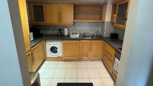 A compact kitchen with wooden cabinets, a washing machine, a sink, and a countertop with various appliances.