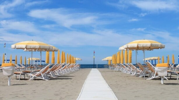 A beach with rows of sun loungers and umbrellas, a white walkway, and the ocean in the background. - Apartment 'La Terrazza di Elisabetta' with Private Terrace, Balcony and Air Conditioning (Viareggio)