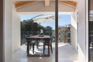 A balcony with a table and chairs, a potted plant, and a large umbrella.