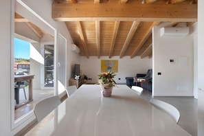 Une pièce spacieuse avec une grande table blanche, des poutres en bois au plafond et une plante en pot.