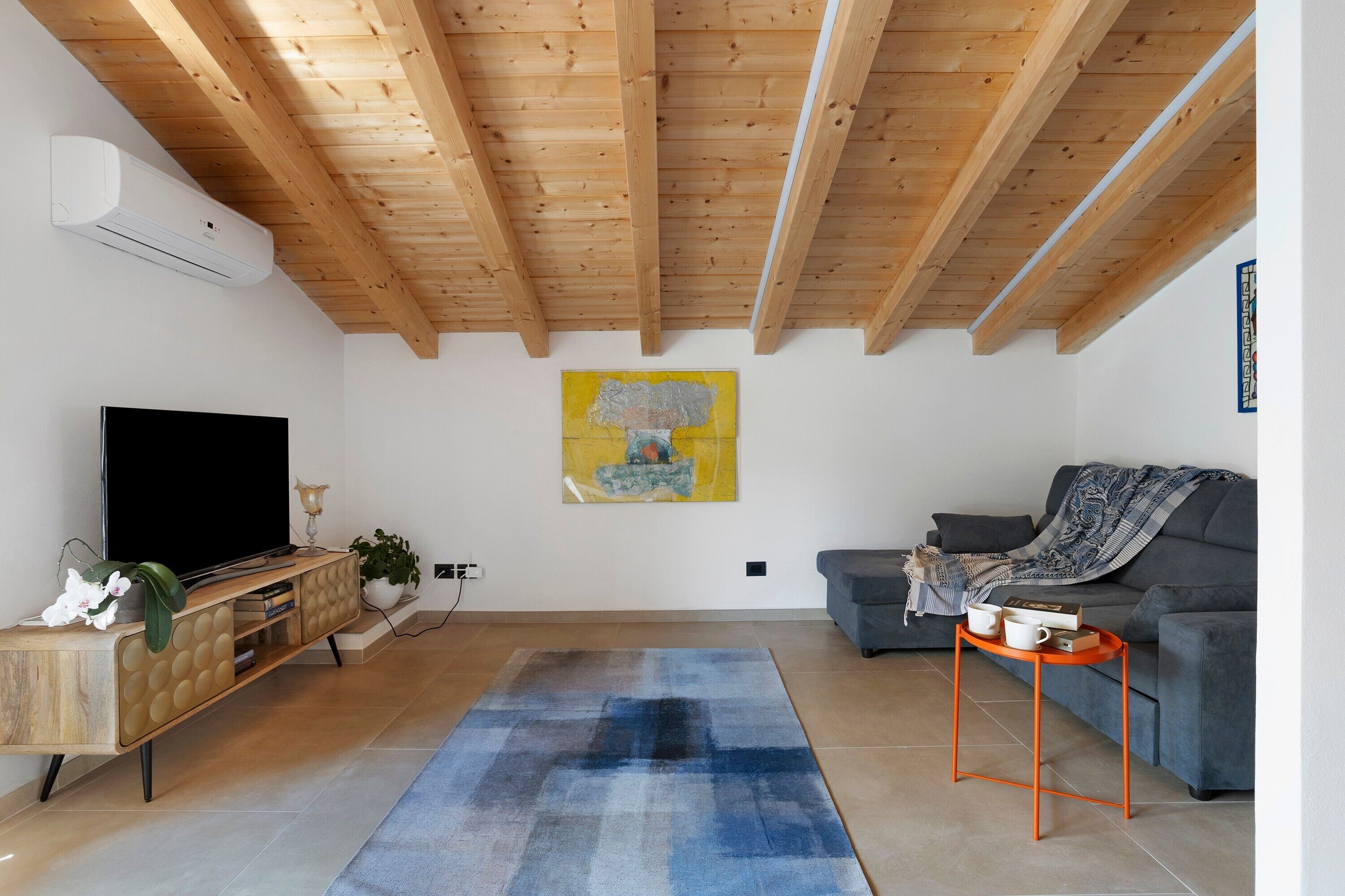 A living room with a wooden ceiling, a flat-screen TV, a sofa, a coffee table, and a painting on the wall.