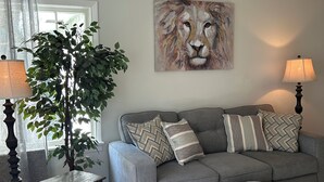 A living room with a grey sofa, a painting of a lion, a lamp, a plant, and a small table.