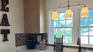 A kitchen with wooden cabinets, a dishwasher, a coffee station, and a window with a view of greenery.