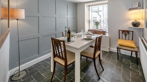 A dining area with a white table, two wooden chairs, a bottle of wine, and a vase with flowers. - 2 Bed in Ilfracombe (oc-f31994) (Ilfracombe)
