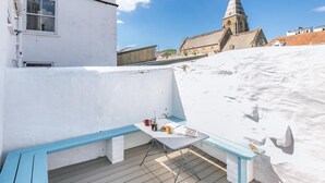 A rooftop terrace with a table, chairs, and a view of a church. - 2 Bed in Ilfracombe (oc-f31994) (Ilfracombe)