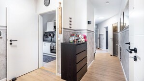 Un couloir avec un meuble de rangement noir, une horloge et une porte donnant sur un espace cuisine.