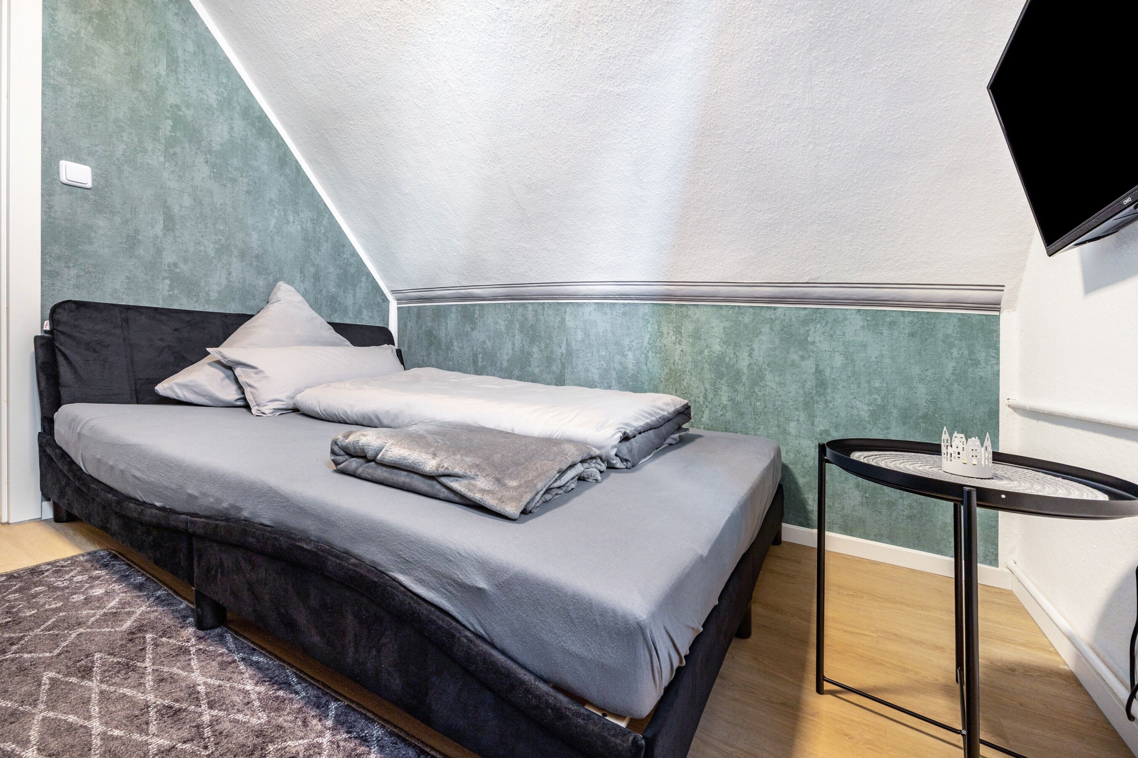 Een slaapkamer met een bed, een klein tafeltje en een tv aan de muur.