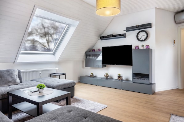 A modern living room with a skylight, grey sofas, a flat-screen TV, and a minimalist design.