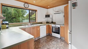 A modern kitchen with wooden cabinets, a built-in oven, a microwave, and a refrigerator. - So Good On Sargood - Wanaka Holiday Home (Wanaka)
