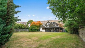 A house with a covered porch, a fenced yard, and a mountain backdrop. - So Good On Sargood - Wanaka Holiday Home (Wanaka)
