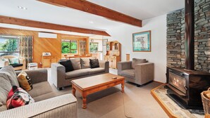 A cozy living room with a fireplace, wooden beams, and a stone wall. - So Good On Sargood - Wanaka Holiday Home (Wanaka)