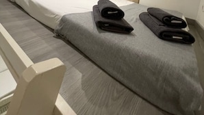 A single bed with a grey blanket and two rolled-up towels.