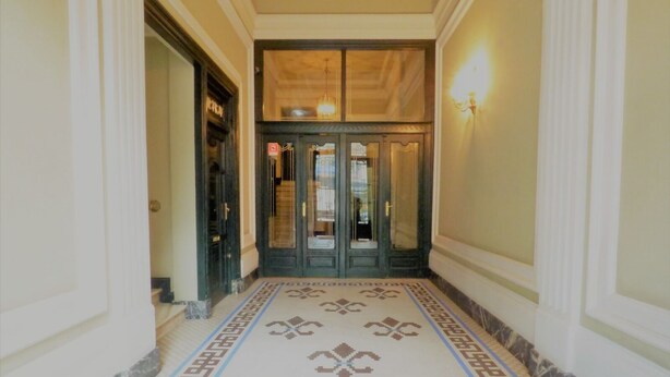 A hallway with a patterned floor, a double door with glass panels, and a wall-mounted light fixture.