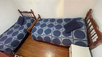 Een kleine, compacte kamer met twee houten bedden, elk voorzien van een matras en kussens met een blauw-wit patroon.