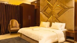 Ein Hotelzimmer mit einem großen Bett, einem Kleiderschrank, einem Sessel und einer dekorativen Wandverkleidung.
