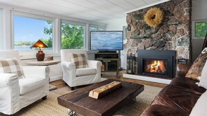 A living room with a stone fireplace, a television, and a view of the outdoors. - Hennessy Lake House, Port Carling Waterfront Property (Port Carling)