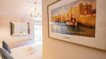 Une chambre d’hôtel avec un lit, un lustre, un grand tableau encadré représentant un port et un miroir au mur.