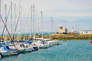 A marina with multiple sailboats docked, a lighthouse, and a stone wall in the background. - Charming Howth Marina Retreat (Dublin)