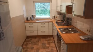 Een kleine keuken met een raam, witte kasten, een fornuis en een vaatwasser.