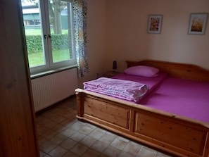 Un dormitorio con una cama de madera, un ventanal con vistas al exterior y un radiador.