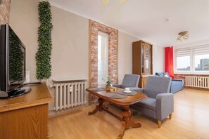 Un salon avec une télévision, un mur en briques, un radiateur, une table avec des sets de table et un canapé gris.