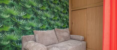 Una habitación con una pared cubierta de hojas verdes, un armario de madera y un sofá beig con almohadones.