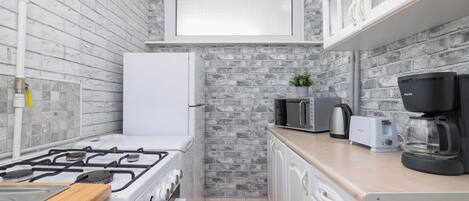 Una cocina compacta con estufa a gas, microondas, tostadora y cafetera.