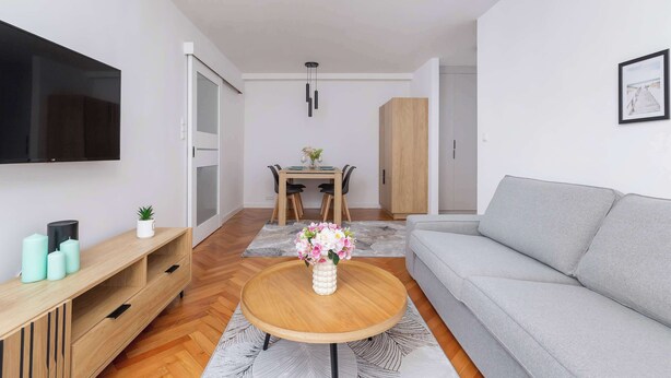 Uma sala de estar moderna com um sofá cinza, mesa de centro de madeira e uma televisão de tela plana na parede.