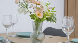 Uma mesa de jantar com um vaso de flores, duas taças de vinho e pratos cor de verde-água.