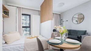 Una habitación de hotel moderna con una cama, un área de comedor con una mesa para dos, un sofá y un ventanal grande.