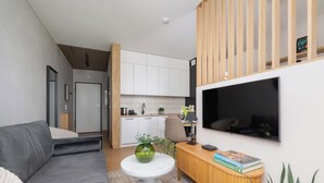 Een moderne woonkamer met een grijze bank, een ronde witte tafel met een groene vaas, een houten console met boeken en een aan de muur bevestigde televisie.