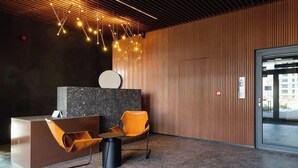 Un área de recepción moderna con un mostrador, un espacio de espera con una silla, un reloj en la pared y un techo con luces colgantes.