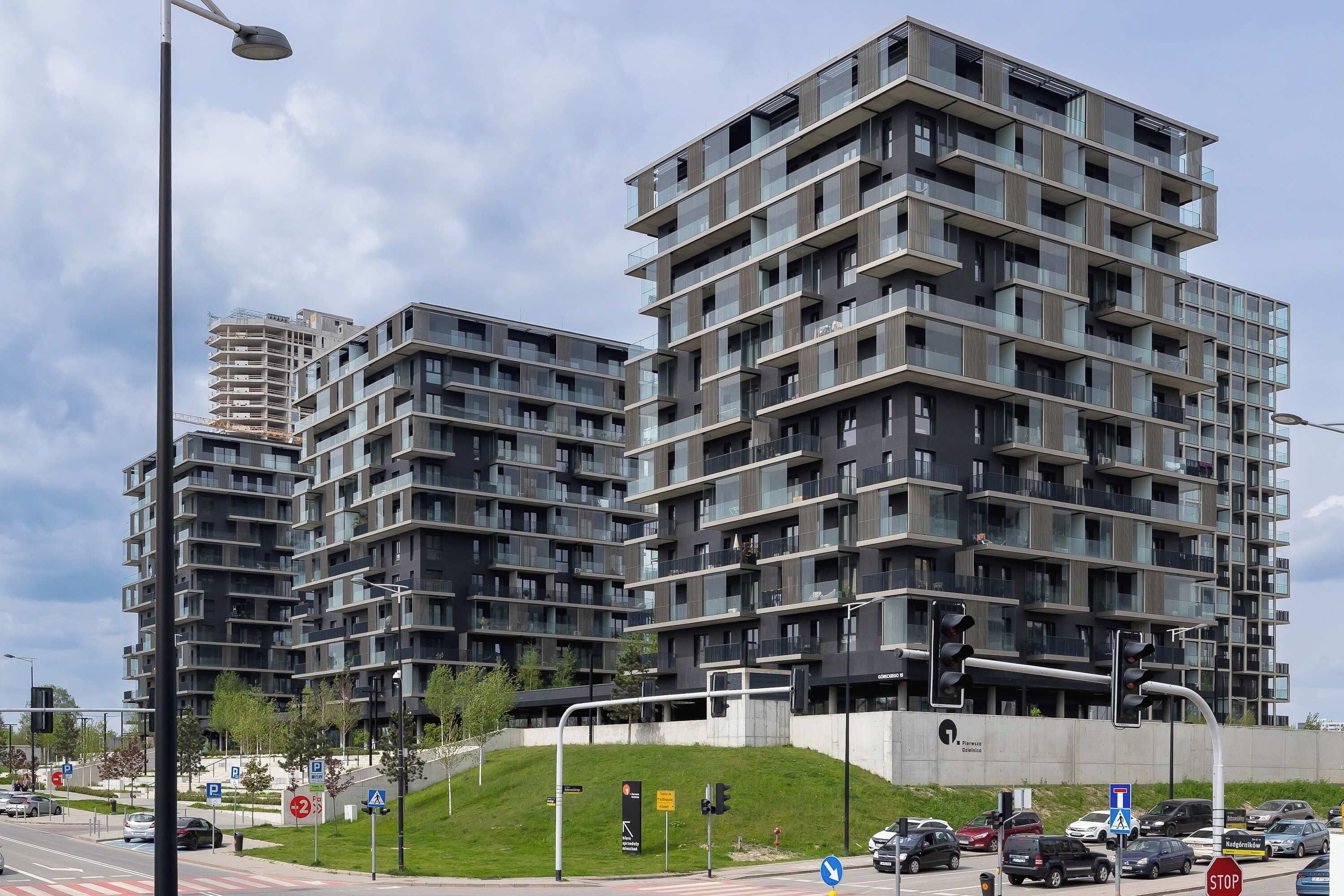 Un edificio residencial moderno de varios pisos con balcones, un área de estacionamiento y un semáforo.