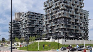 Een modern meerlaags appartementencomplex met balkons, een parkeerplaats en een verkeerslicht.