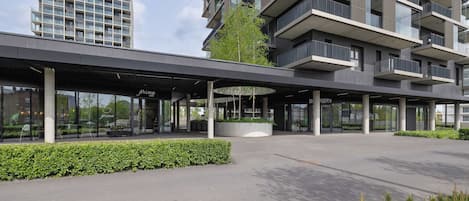 Un edificio moderno con entrada cubierta, ventanas de vidrio y un área ajardinada con vegetación.
