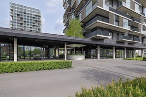 A modern building with a covered entrance, glass windows, and a landscaped area with greenery.