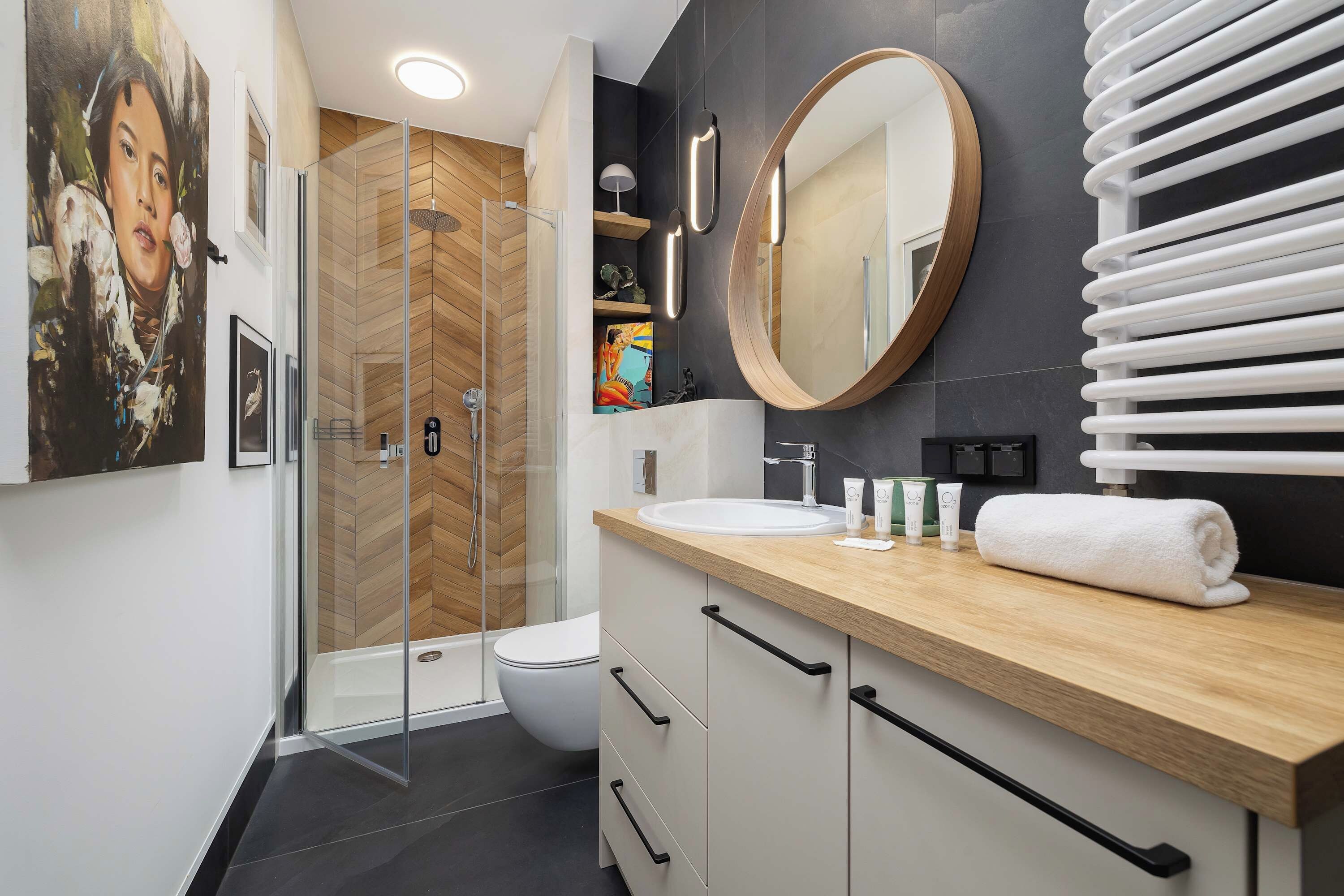 A modern bathroom with a glass shower enclosure, a wooden vanity, a large mirror, and a towel rack.